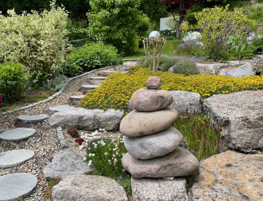 Ein Hanggarten wird Terrassen aus Naturstein stabilisiert und Sträucher ung Blumen steigern die Energie im Garten.